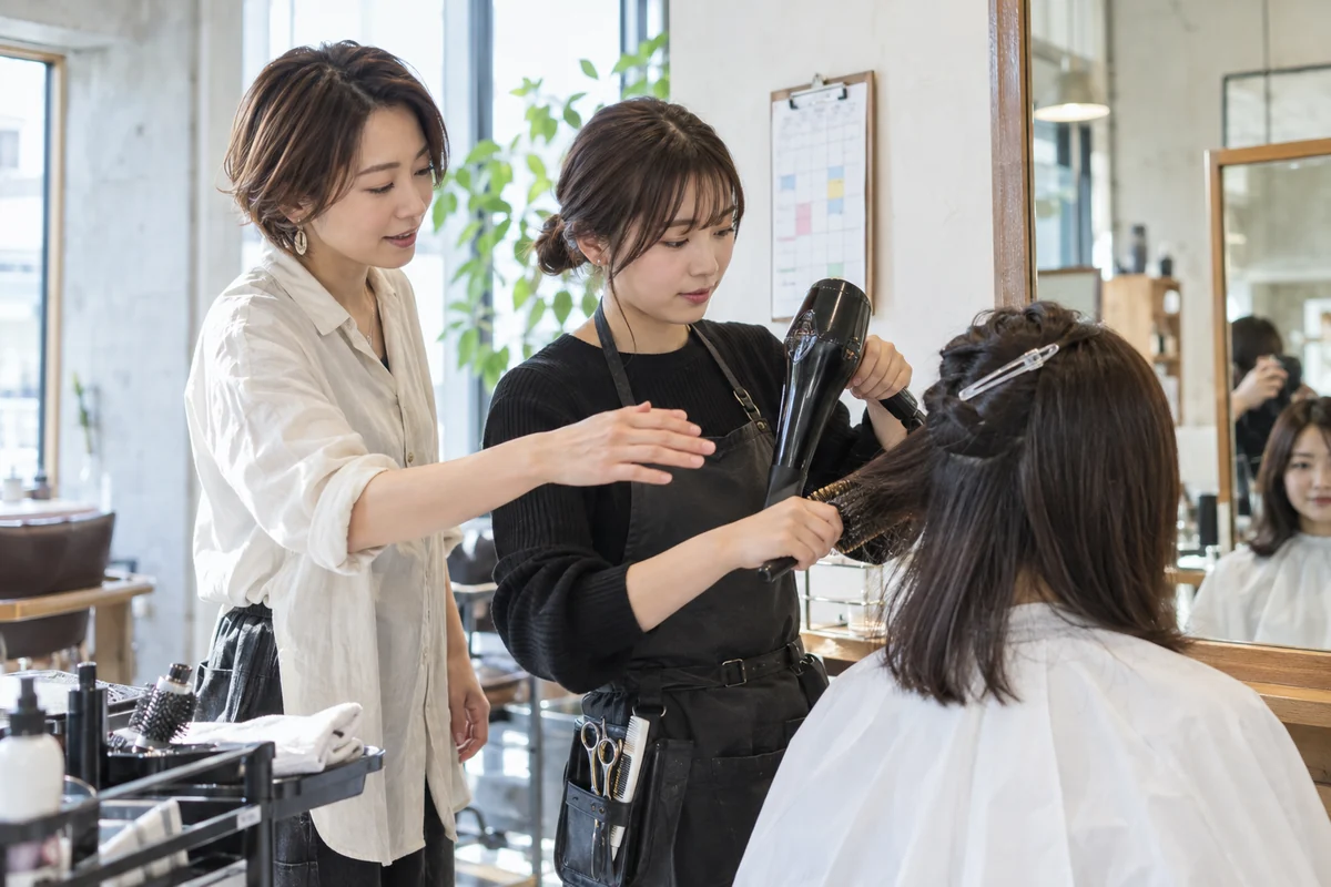 美容室の事業主が新しいスタッフに施術を教えるAI生成の架空イメージ