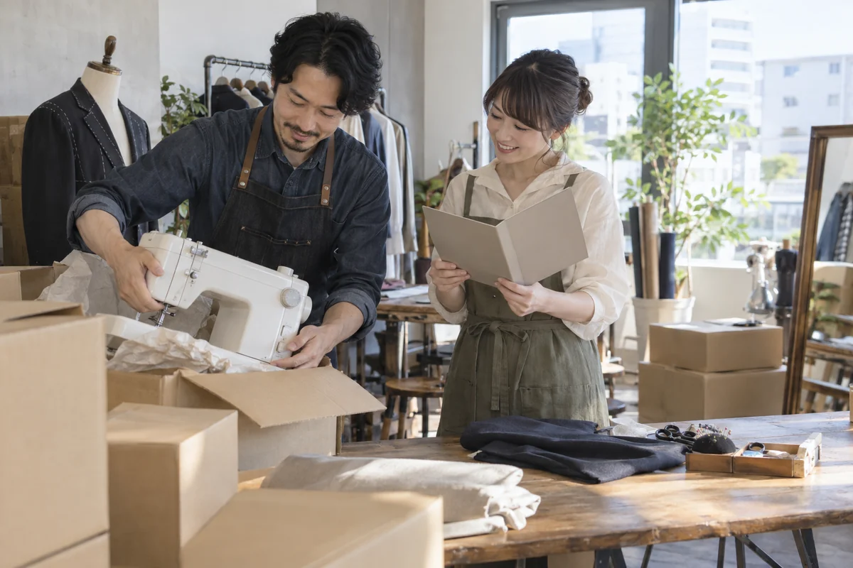 移転する洋裁店の事業主が新しい仕事場でミシンと住所変更資料を確認するAI生成の架空イメージ