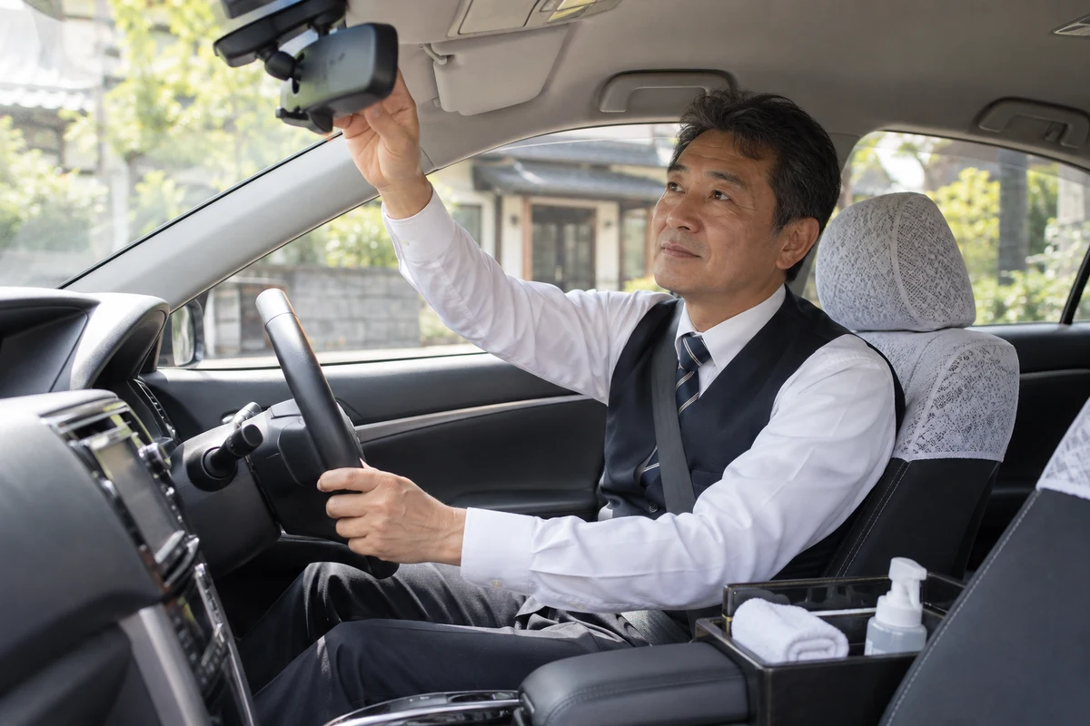 停車した車内でミラーを確認するタクシー運転手。AI生成イメージ