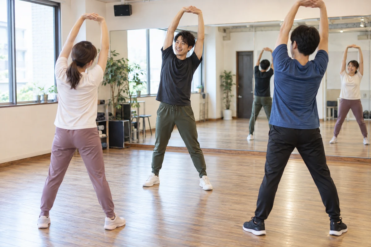 明るいダンススタジオで成人の受講者に準備運動を指導する講師の架空の場面(AI生成)