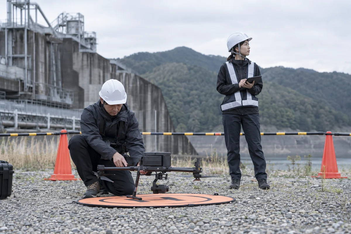 屋外点検の前に機体と飛行区域を確認する日本人ドローン操縦者と補助者を表したAI生成の架空イメージ